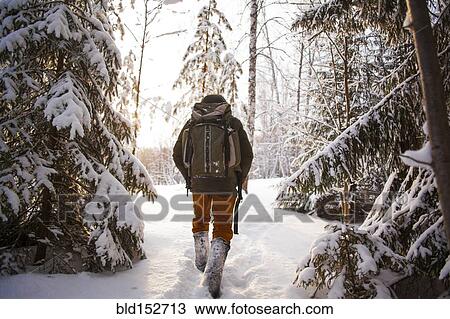 Stock Image - Mixed race man walking in snowy forest. Fotosearch
