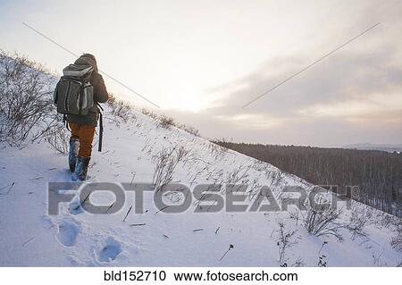 Stock Image - Mixed race man walking on snowy hillside. Fotosearch