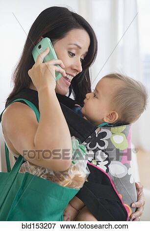 Mixed race mother carrying baby and talking on cell phone View Large Photo Image Stock Photo - Mixed race mother carrying baby and talking on cell phone. Fotosearch