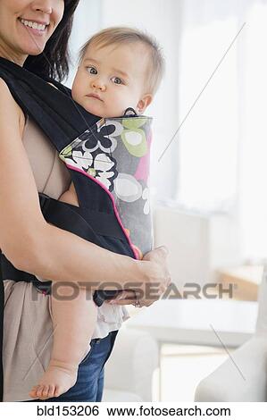 Stock Photograph - Mixed race mother carrying baby in baby carrier. Fotosearch