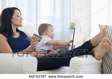 Mixed race mother holding baby and shopping on laptop View Large Photo Image Stock Photo - Mixed race mother holding baby and shopping on laptop. Fotosearch