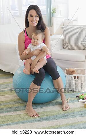 Stock Image - Mixed race mother holding baby on fitness ball. Fotosearch