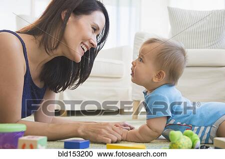 Stock Image - Mixed race mother playing with baby on floor. Fotosearch
