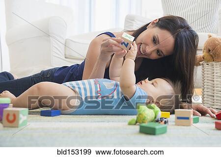 Stock Photo - Mixed race mother playing with baby on floor. Fotosearch
