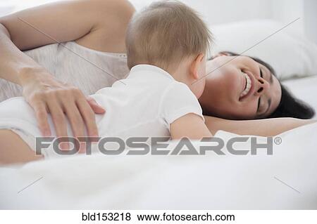 Stock Photo - Mixed race mother playing with baby on bed. Fotosearch
