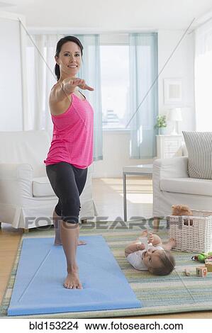 Picture - Mixed race mother practicing yoga and watching baby at home. Fotosearch