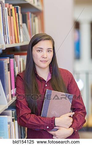 Stock Photography - Mixed race student holding book in library. Fotosearch