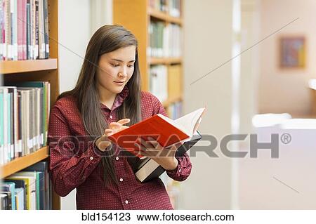 Stock Image - Mixed race student reading in library. Fotosearch