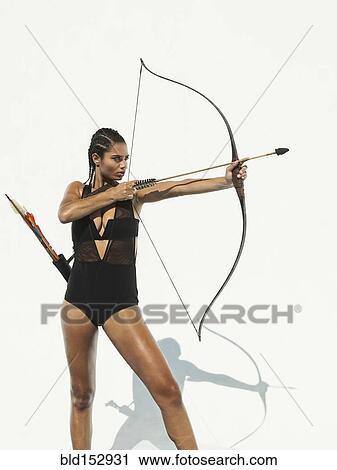 Stock Image - Mixed race woman aiming bow and arrow. Fotosearch