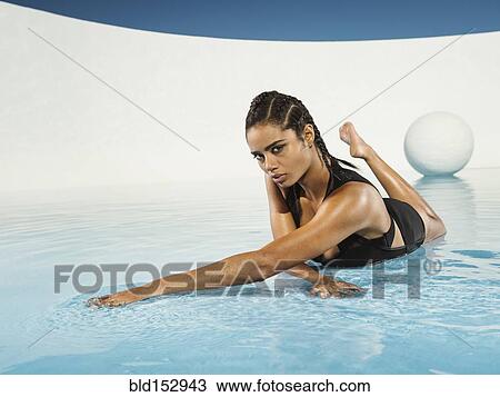 Stock Image - Mixed race woman laying on swimming pool surface. Fotosearch