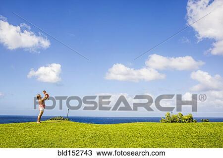 Stock Image - Mother and child playing in grass field under blue sky. Fotosearch