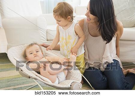Stock Photography - Mother and daughter admiring baby on living room floor. Fotosearch