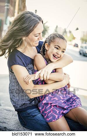 Stock Image - Mother and daughter hugging on sidewalk. Fotosearch