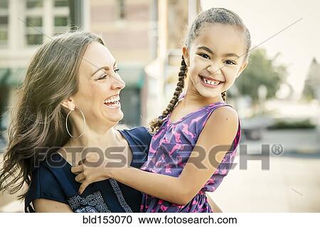 Stock Image - Mother carrying smiling daughter outdoors. Fotosearch
