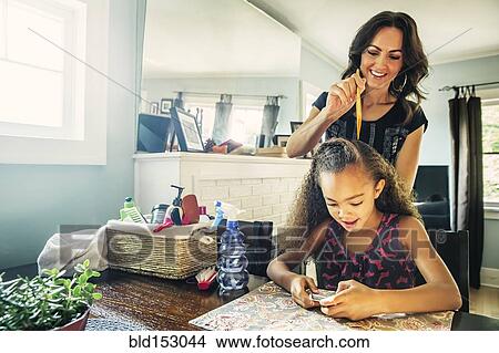Mother combing hair of daughter at kitchen table View Large Photo Image Picture - Mother combing hair of daughter at kitchen table. Fotosearch
