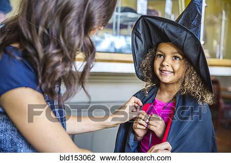 Stock Image - Mother dressing daughter in witch costume. Fotosearch