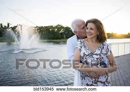 Stock Photography - Older Caucasian couple hugging by fountain. Fotosearch