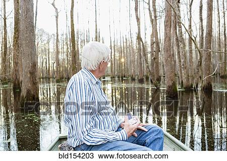 Stock Image - Older Caucasian man riding boat in swamp. Fotosearch