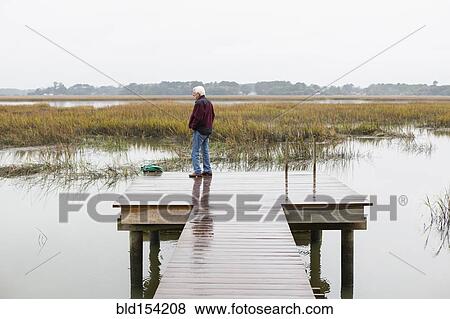 Stock Photo - Older Caucasian man standing on wooden dock over lake. Fotosearch