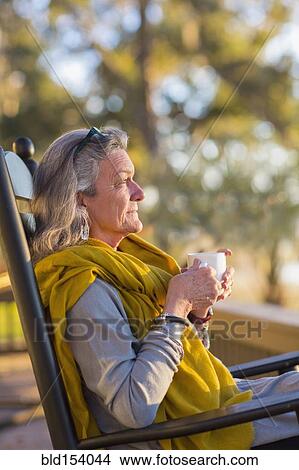 Picture - Older Caucasian woman drinking coffee in rocking chair. Fotosearch