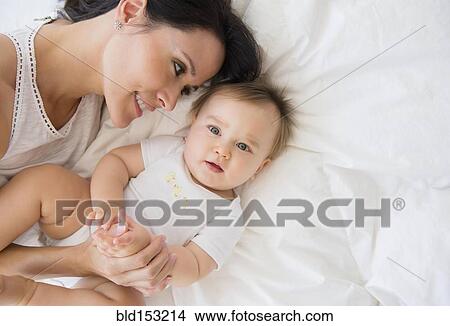 Overhead view of mixed race mother laying with baby on bed View Large Photo Image Picture - Overhead view of mixed race mother laying with baby on bed. Fotosearch