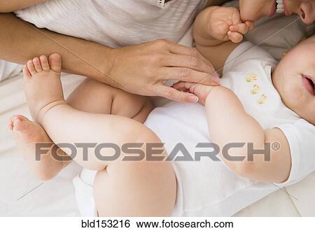 Stock Photograph - Overhead view of mixed race mother laying with baby on bed. Fotosearch