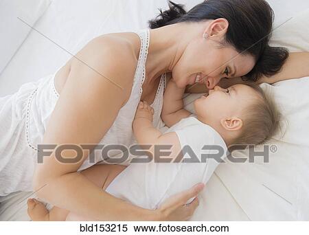 Stock Photography - Overhead view of mixed race mother laying with baby on bed. Fotosearch
