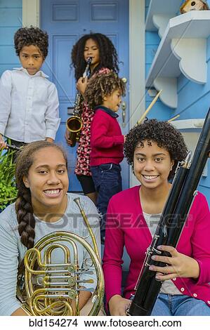 Picture - Pacific Islander family holding musical instruments on front stoop. Fotosearch
