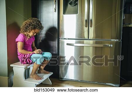Stock Photo - Sad mixed race girl sitting near refrigerator. Fotosearch