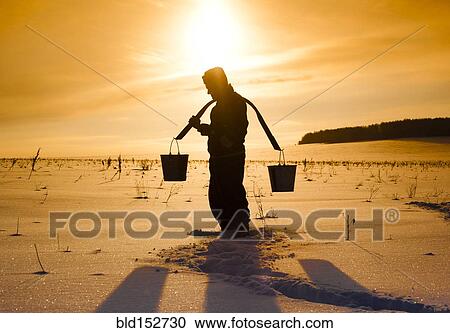 Stock Image - Silhouette of Mari man carrying buckets on traditional yoke in snowy field. Fotosearch