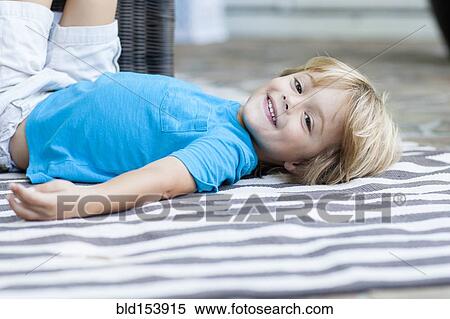 Stock Photography - Smiling Caucasian boy laying on rug. Fotosearch