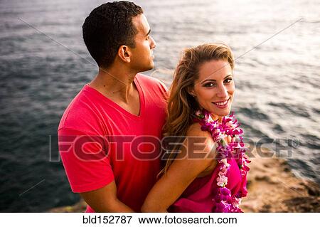 Stock Photo - Smiling couple hugging on rocks over ocean. Fotosearch