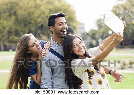 Smiling friends taking photograph with digital tablet in park View Large Photo Image Stock Image - Smiling friends taking photograph with digital tablet in park. Fotosearch