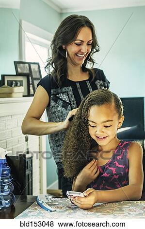 Stock Photo - Smiling mother brushing hair of daughter. Fotosearch