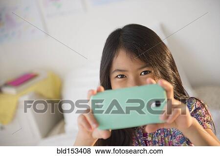 Stock Photo - Smiling Vietnamese girl taking cell phone photograph. Fotosearch