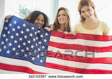Smiling women holding American flag View Large Photo Image Stock Photo - Smiling women holding American flag. Fotosearch