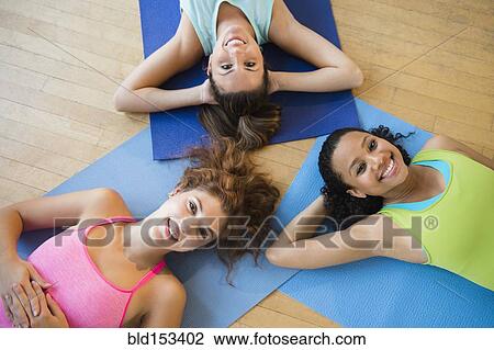 Stock Image - Smiling women laying on exercise mats in studio. Fotosearch