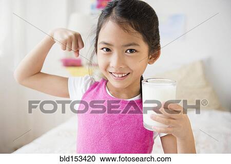 Stock Image - Vietnamese girl flexing muscles with glass of milk. Fotosearch