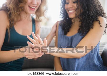 Stock Photograph - Woman admiring engagement ring of friend. Fotosearch