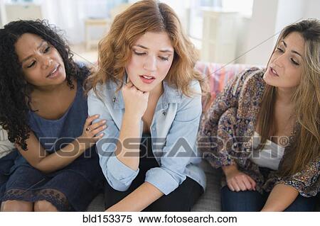 Stock Photography - Women comforting sad friend on sofa in living room. Fotosearch