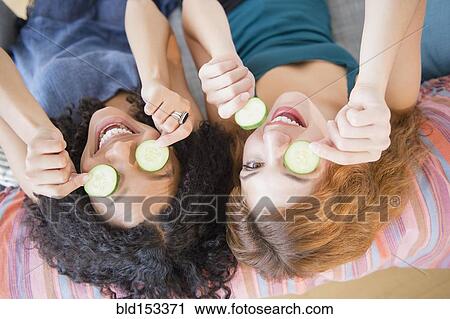 Women holding cucumber slices over eyes View Large Photo Image Stock Image - Women holding cucumber slices over eyes. Fotosearch
