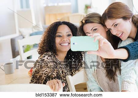 Stock Photo - Women taking cell phone photograph in dining room. Fotosearch
