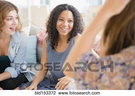 Stock Image - Women talking on sofa in living room. Fotosearch