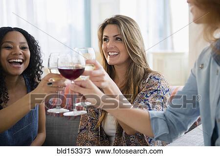 Women toasting each other with wine in living room View Large Photo Image Stock Image - Women toasting each other with wine in living room. Fotosearch