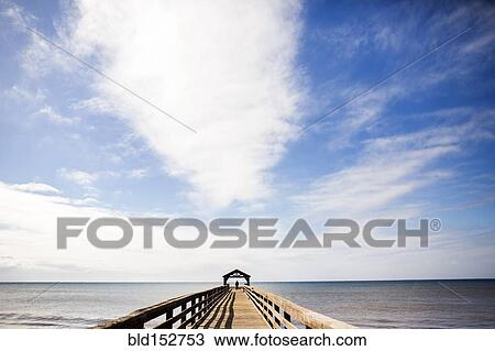 Stock Image - Wooden pier under blue sky over ocean. Fotosearch