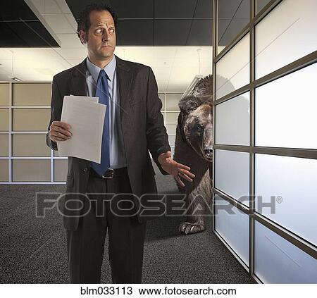 Stock Image - Bear stalking nervous businessman in office. Fotosearch