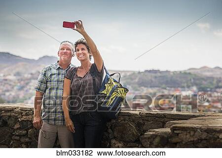 Stock Image - Caucasian couple taking cell phone photograph together on rooftop. Fotosearch