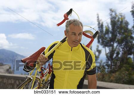 Stock Image - Caucasian cyclist carrying bicycle on remote coastal road. Fotosearch