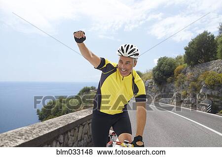Stock Photo - Caucasian cyclist cheering on remote coastal road. Fotosearch