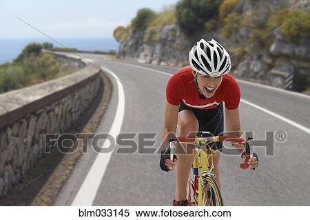 Stock Photography - Caucasian cyclist cheering on remote coastal road. Fotosearch